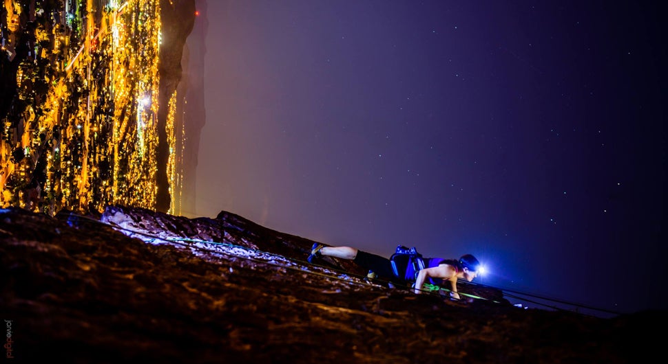 Spectacular photo of a woman climbing a vertical rock wall at night