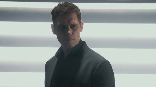 Joseph Morgan as James Ackerson stands against a brightly lit wall. 