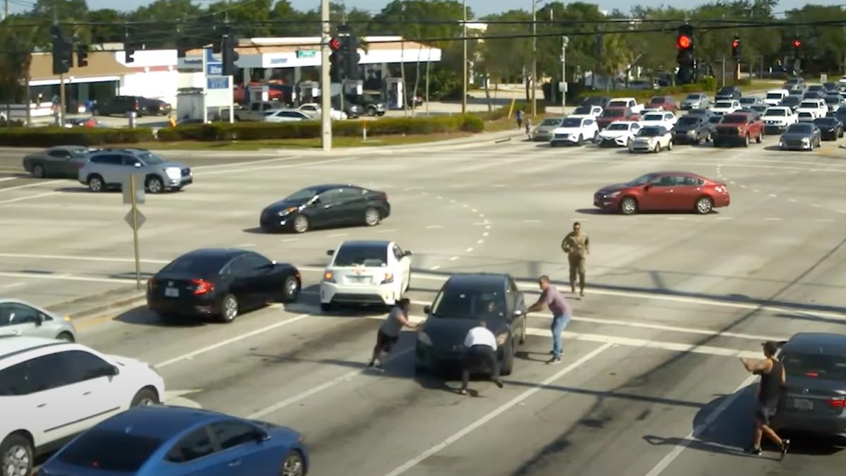 Mehrere Autofahrer eilen zu Fuß über eine belebte Kreuzung, um einen nicht ansprechbaren Fahrer zu retten