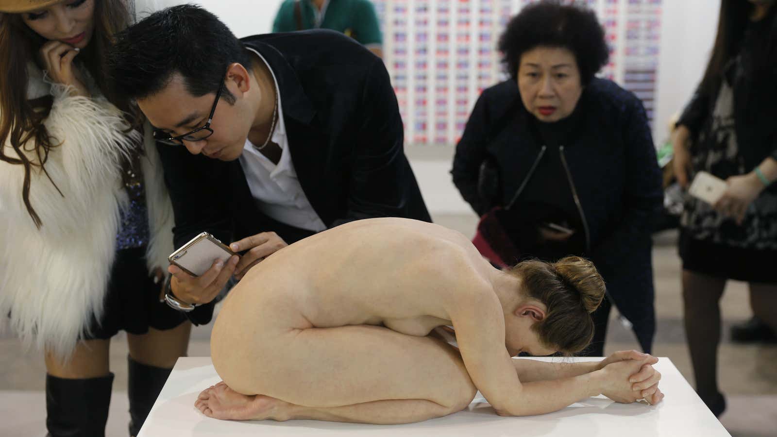 Visitors photograph “Untitled (Kneeling Woman),” a sculpture made by Sam Jinks with silicone and human hair, at Hong Kong’s Art Basel.