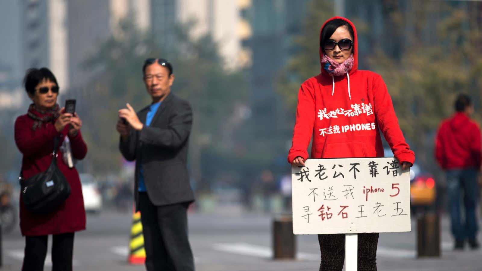 Near a new Apple store in Beijing, a woman holds a sign that says “My husband is not reliable, (he) doesn’t buy me an iPhone 5, (I’m) looking for a rich man”