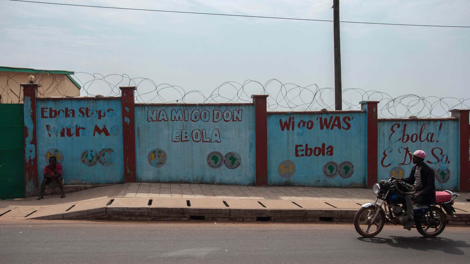 Men on motorbikes pass a wall with ‘We go wash Ebola’ in Freetown, Sierra Leone.