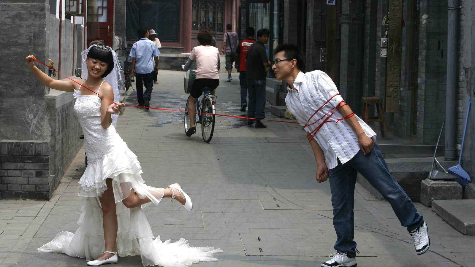 A Chinese couple pose for a wedding photo on a busy alleyway or ‘hutong’ in Beijing July 7, 2008. Marriage registration offices in Beijing predict…