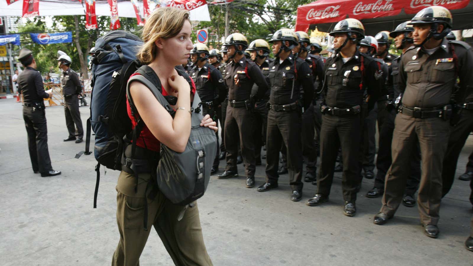 A tourist walks past policemen in Bangkok.