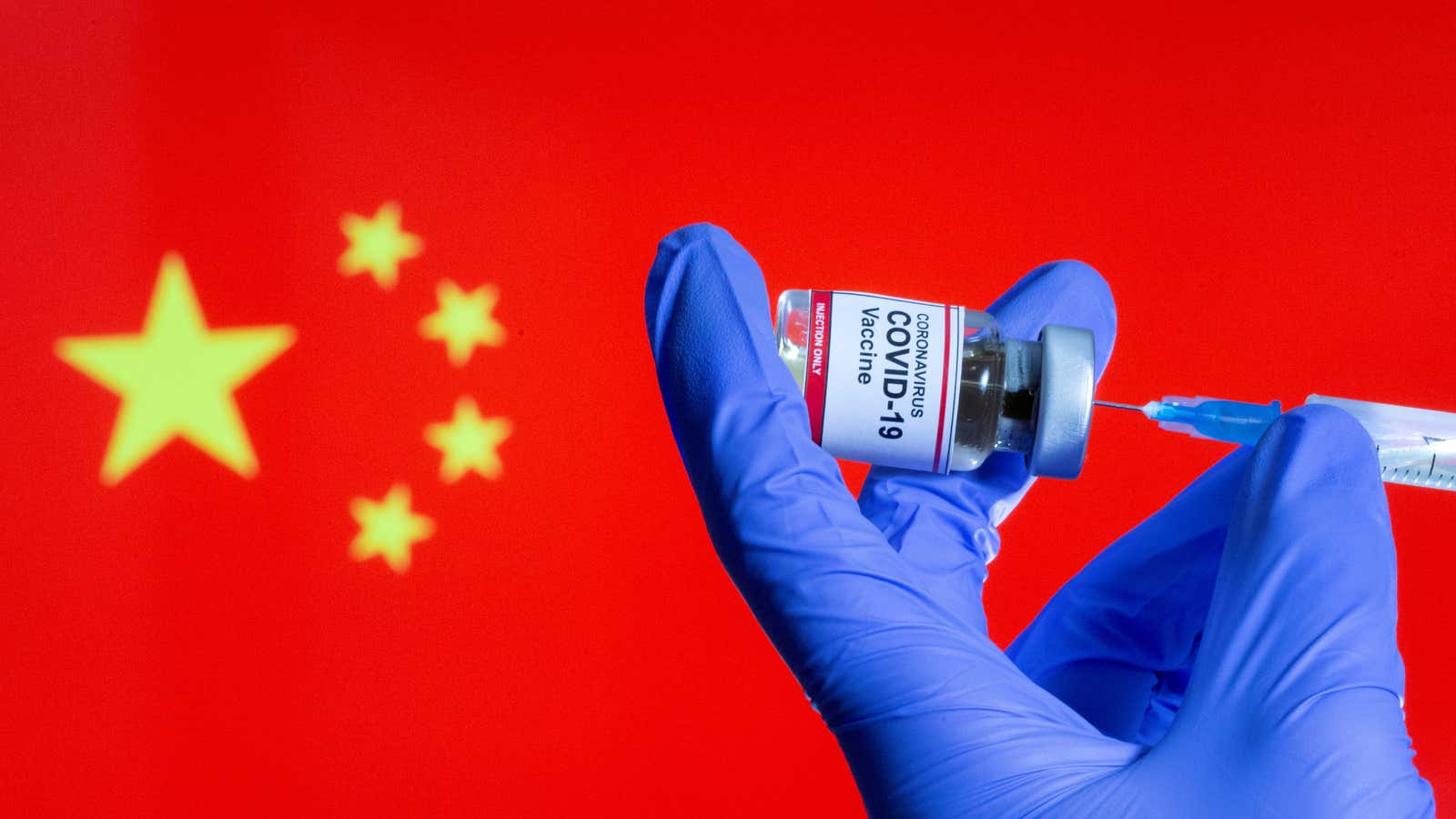 FILE PHOTO: A woman holds a small bottle labeled with a “Coronavirus COVID-19 Vaccine” sticker and a medical syringe in front of displayed China flag…