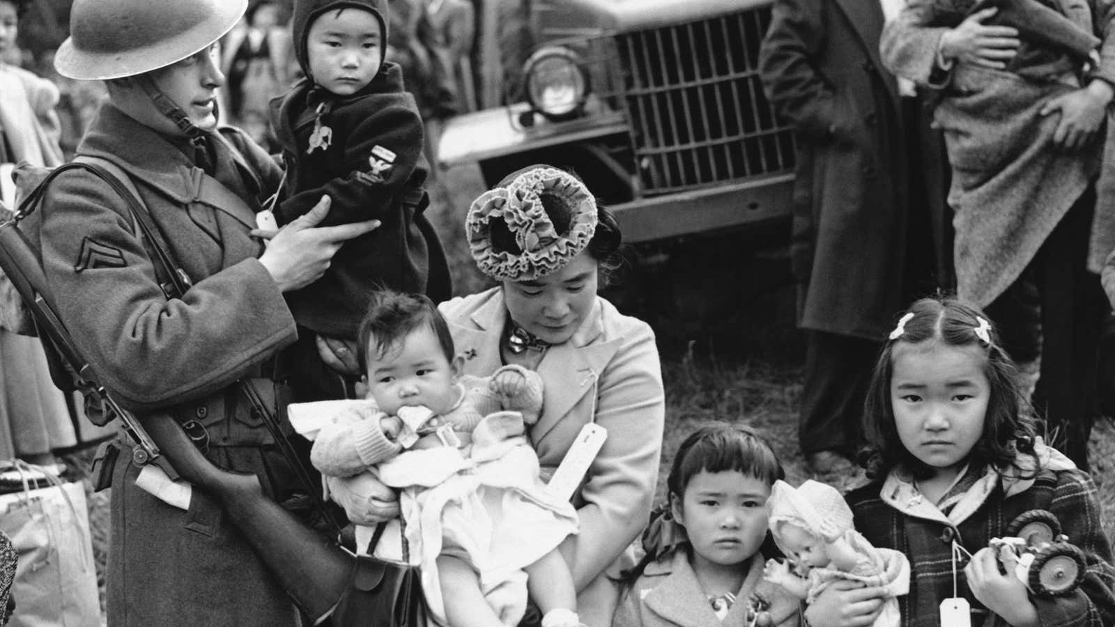 A member of the military guard holds the youngest child of Shigeho Kitamoto, center, as she and her children are evacuated from Bainbridge Island, WA, in March of 1942.