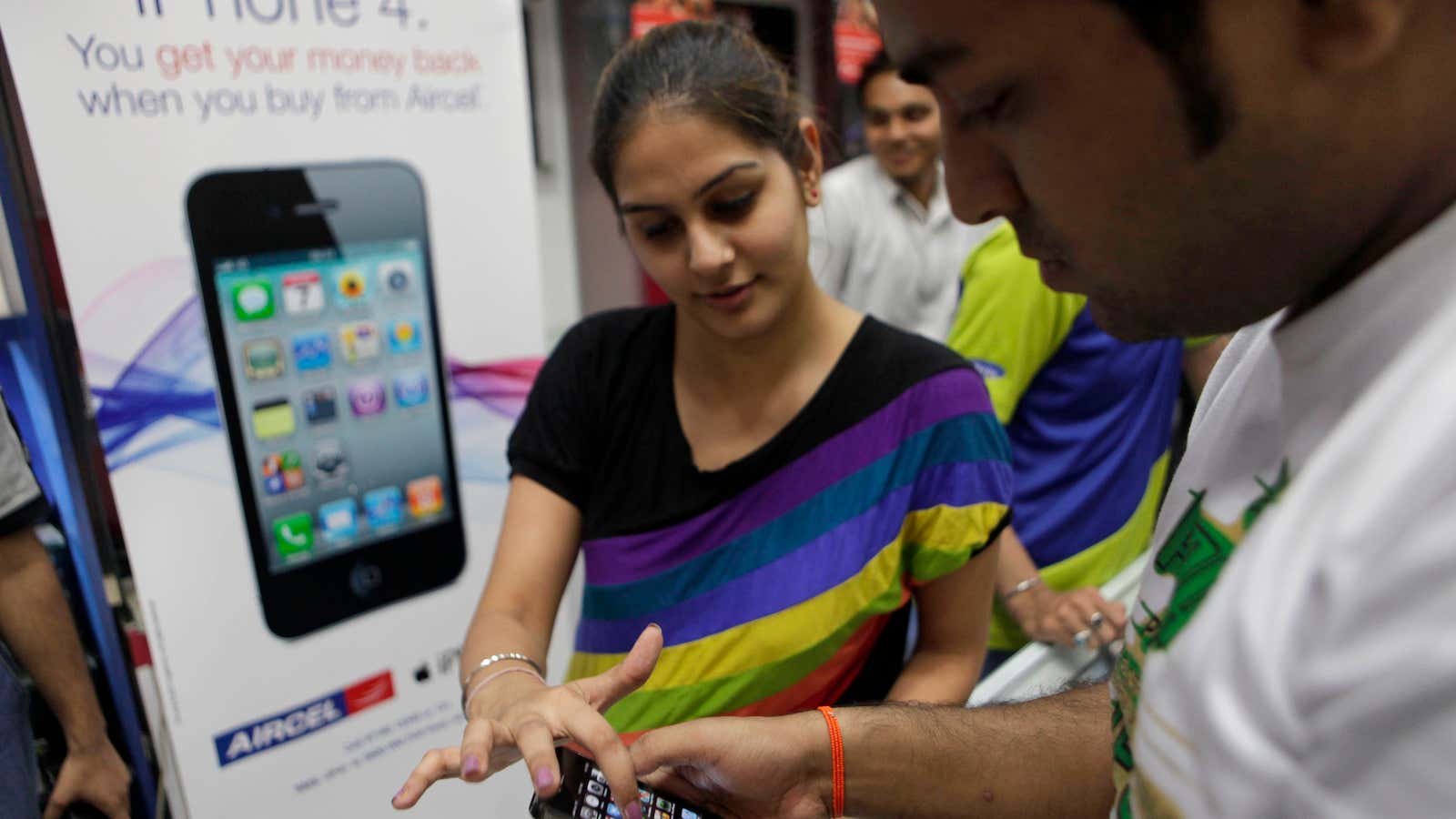 A salesgirl at a mobile phone shop helps a customer with the working of the Apple iPhone 4 in New Delhi, India, Friday, May 27,…