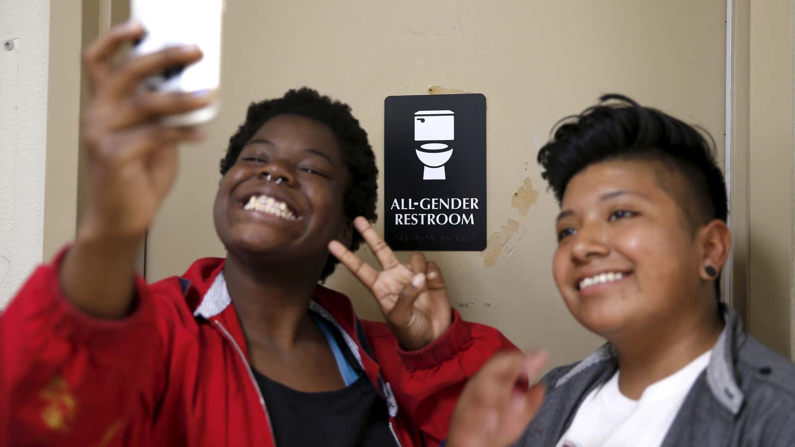 Kween Robinson, 17, (L) and Alonzo Hernandez, 16, pose for a selfie in front of the first gender-neutral restroom in the Los Angeles school district. The US still does not know how many trans and gender-nonconforming kids go to its high schools, but it is finally about to find out