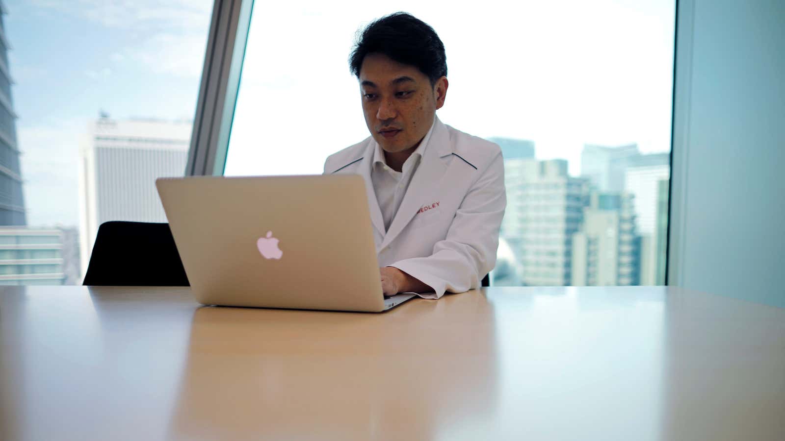 A doctor in a white lab coat sits in front of a laptop.