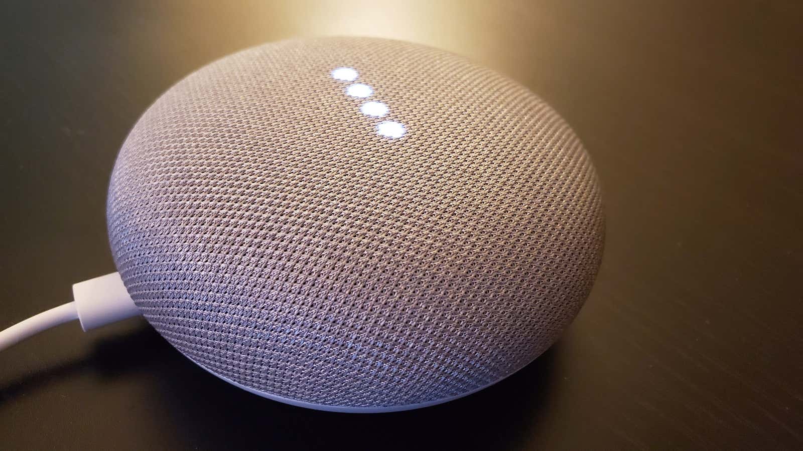 A Google Home smart speaker, which is a rounded gray cylinder with several white lights glowing within.