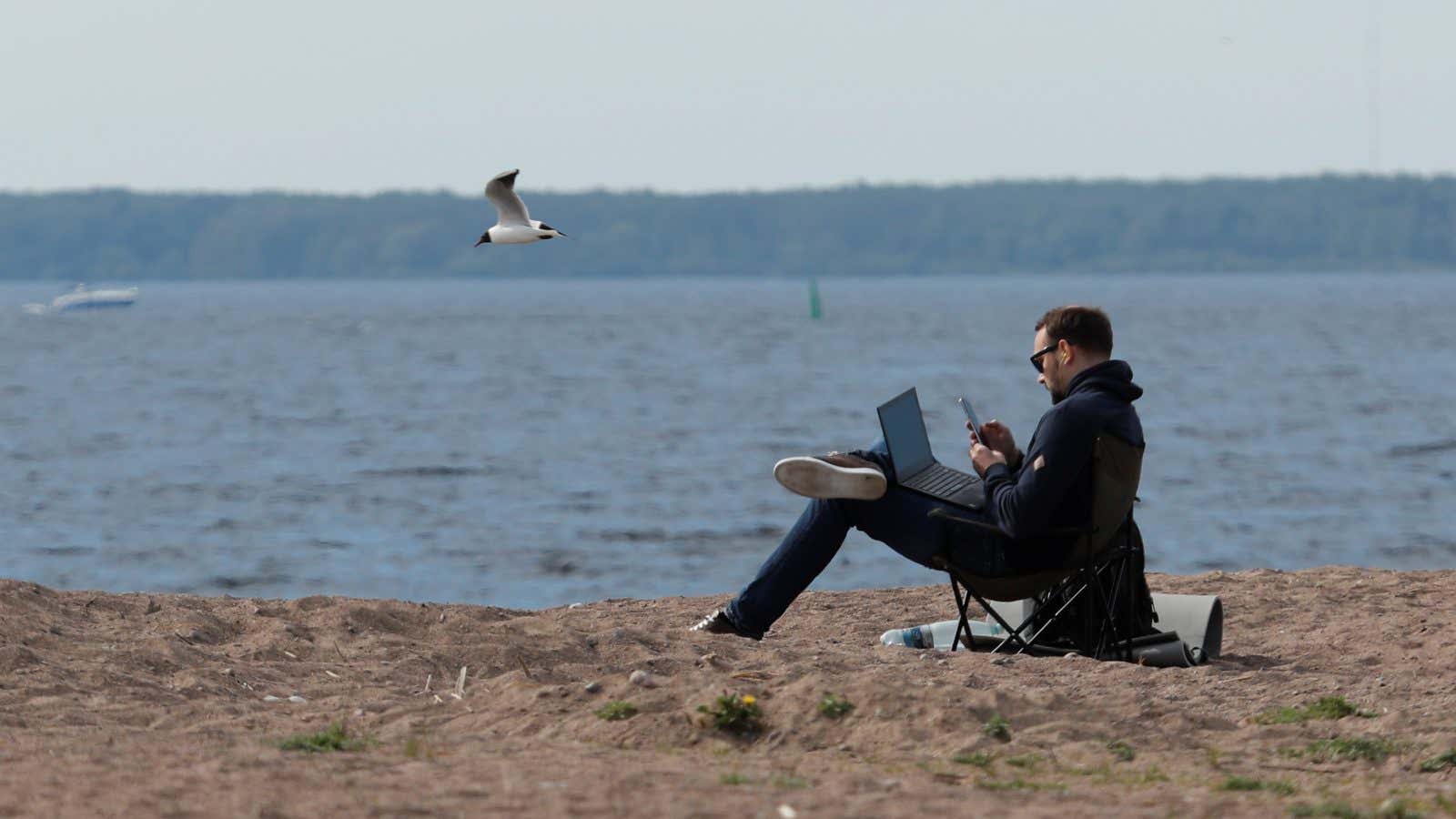 A man uses his smartphone and laptop as he sits on the shore of the Gulf of Finland amid the outbreak of the coronavirus disease…