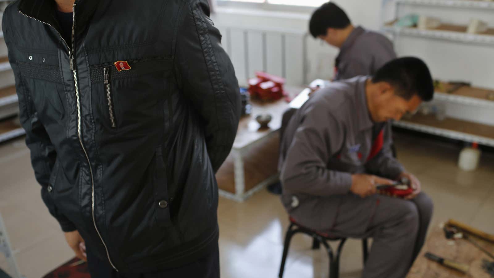 North Korean workers make soccer shoes as a North Korean manager stands supervising inside a temporary factory at a rural village on the edge of Dandong, China.
