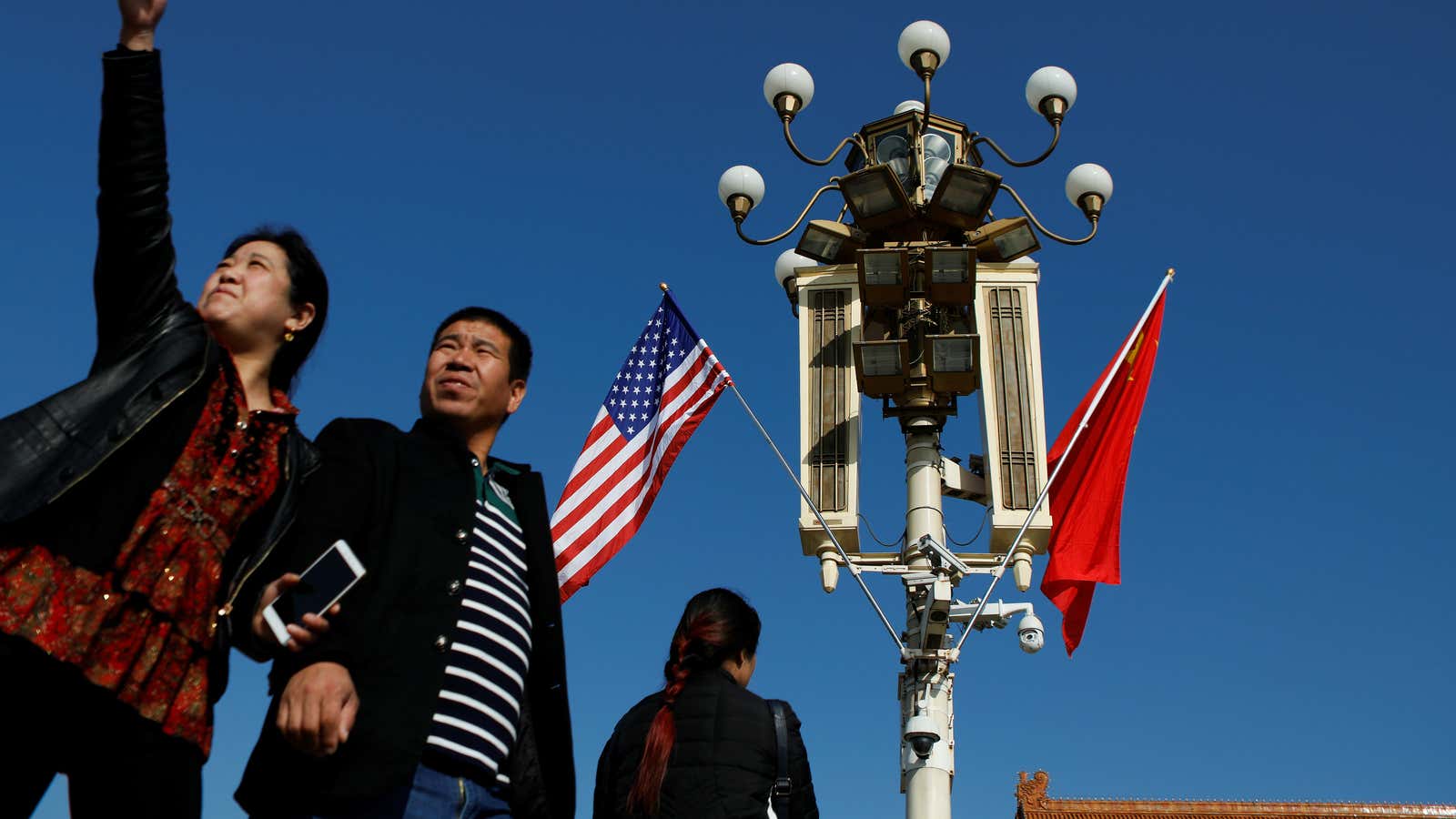 People pass under a pole with security cameras, U.S. and China’s flags near the Forbidden City ahead of the visit by U.S. President Donald Trump…
