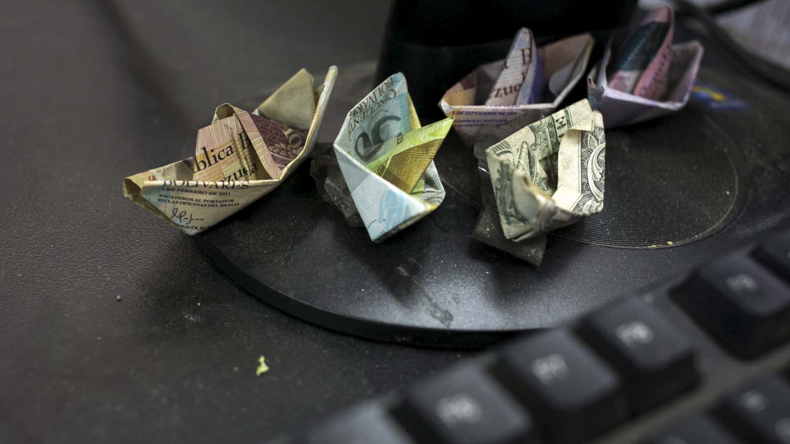Venezuelan bolivar banknotes and a U.S. dollar banknote, folded as boats, are seen at a fruit and vegetable store in Caracas July 10, 2015. Origami-like…