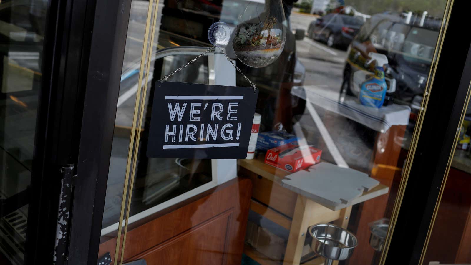 A sign hangs in a shop window reading “We’re hiring!”