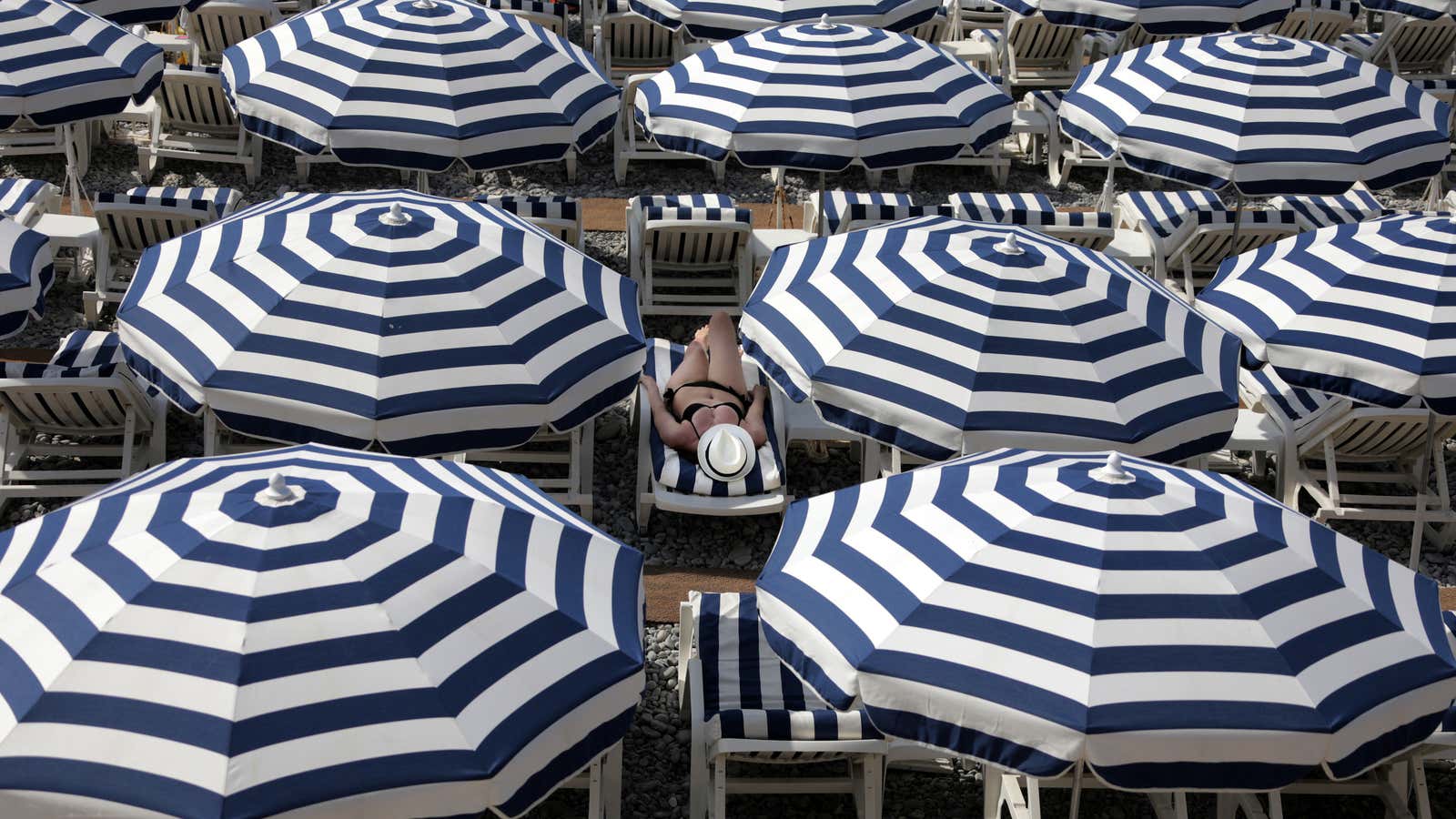 A tourist enjoys the sun on a beach covered with umbrellas on the Promenade Des Anglais during a sunny summer day in Nice, France, July…