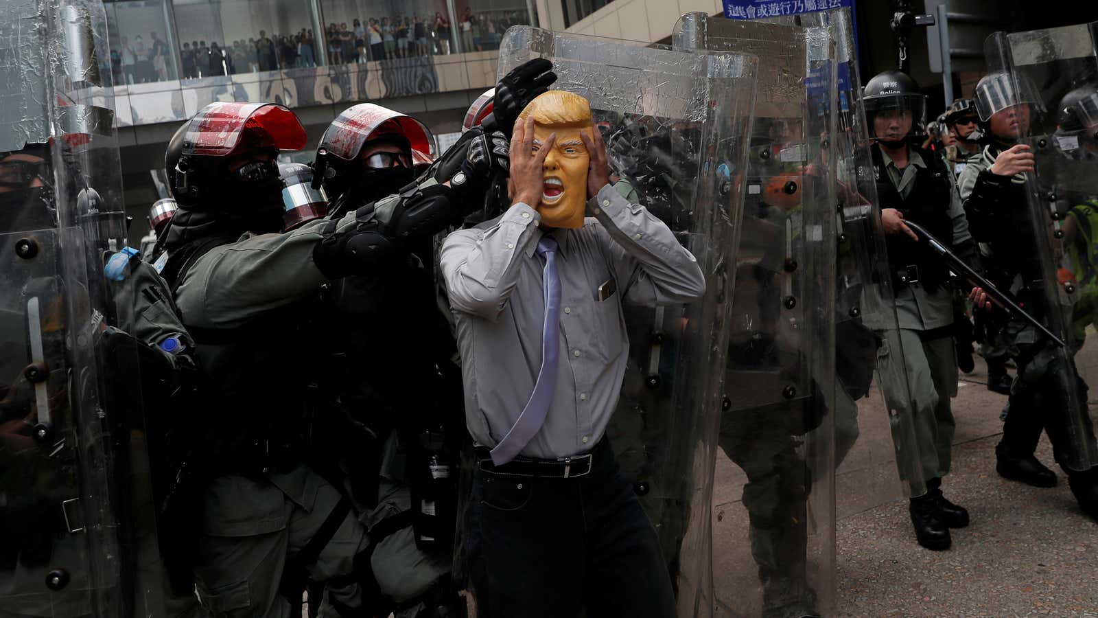 An anti-government protester wearing a mask depicting U.S. President Donald Trump is pushed away by riot police during a demonstration at Causeway Bay district in…