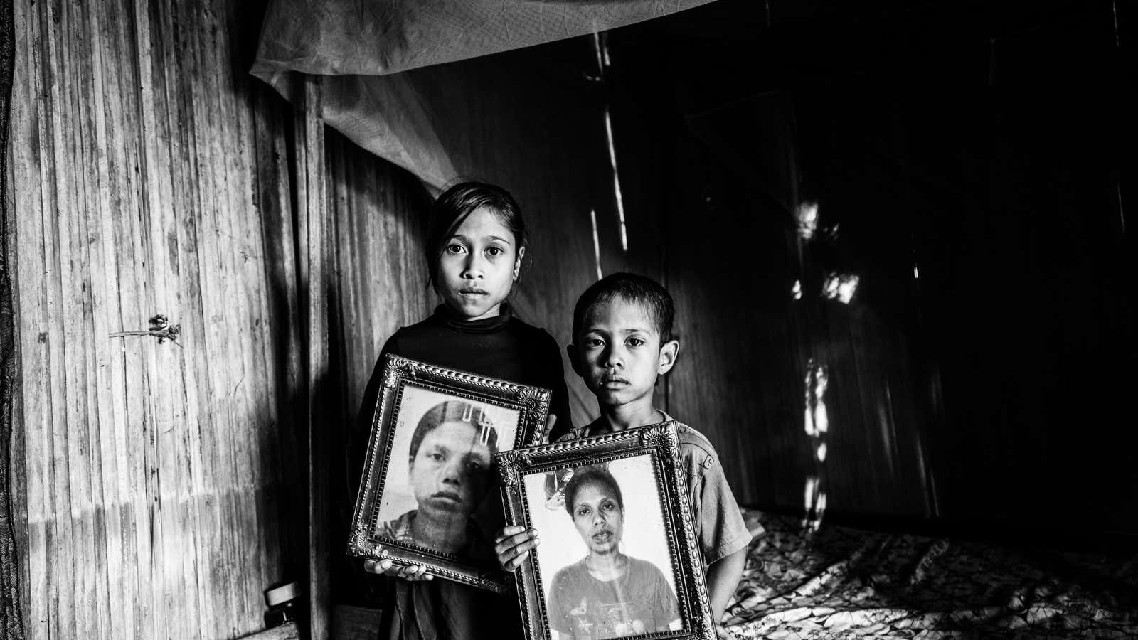 Dolfina’s children Erna and Julius hold photos of their mother inside their hut in East Nusa Tenggara, Indonesia. They now live with their grandfather Mikhael.