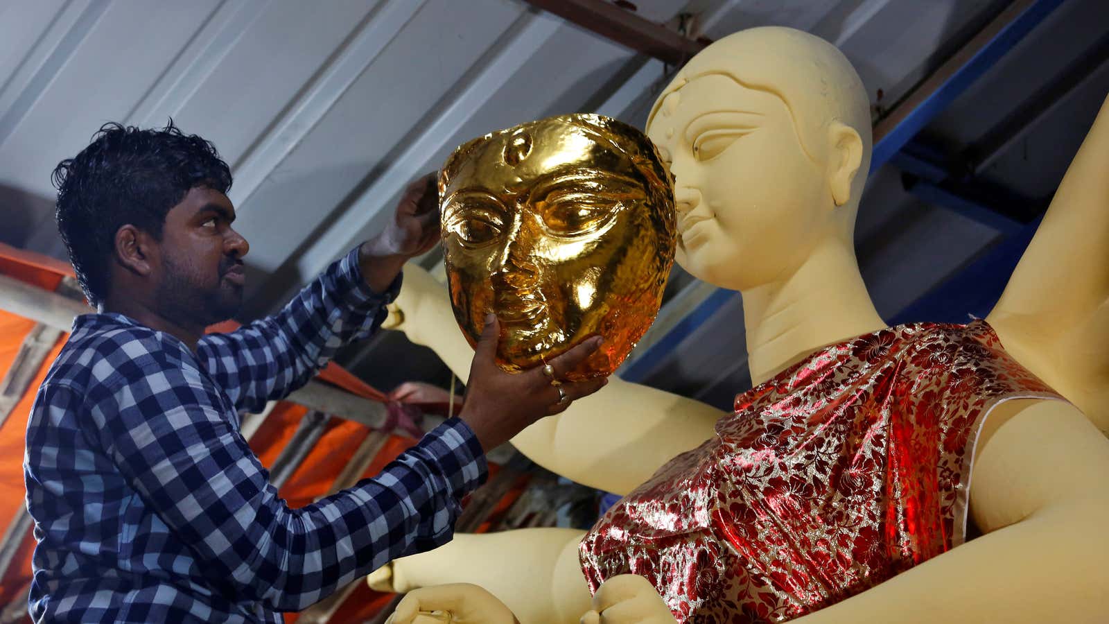 An artisan tries a gold face on an idol of the Hindu goddess Durga during a media preview inside a workshop during preparations for the…