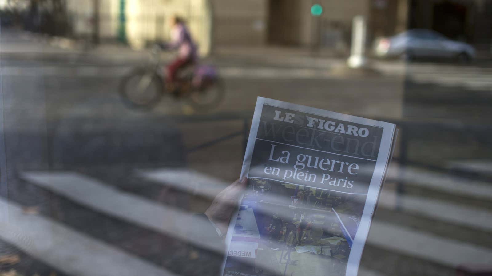 A man reads a newspaper with a headline reading “War in the heart of Paris” in a hotel lobby in Paris.