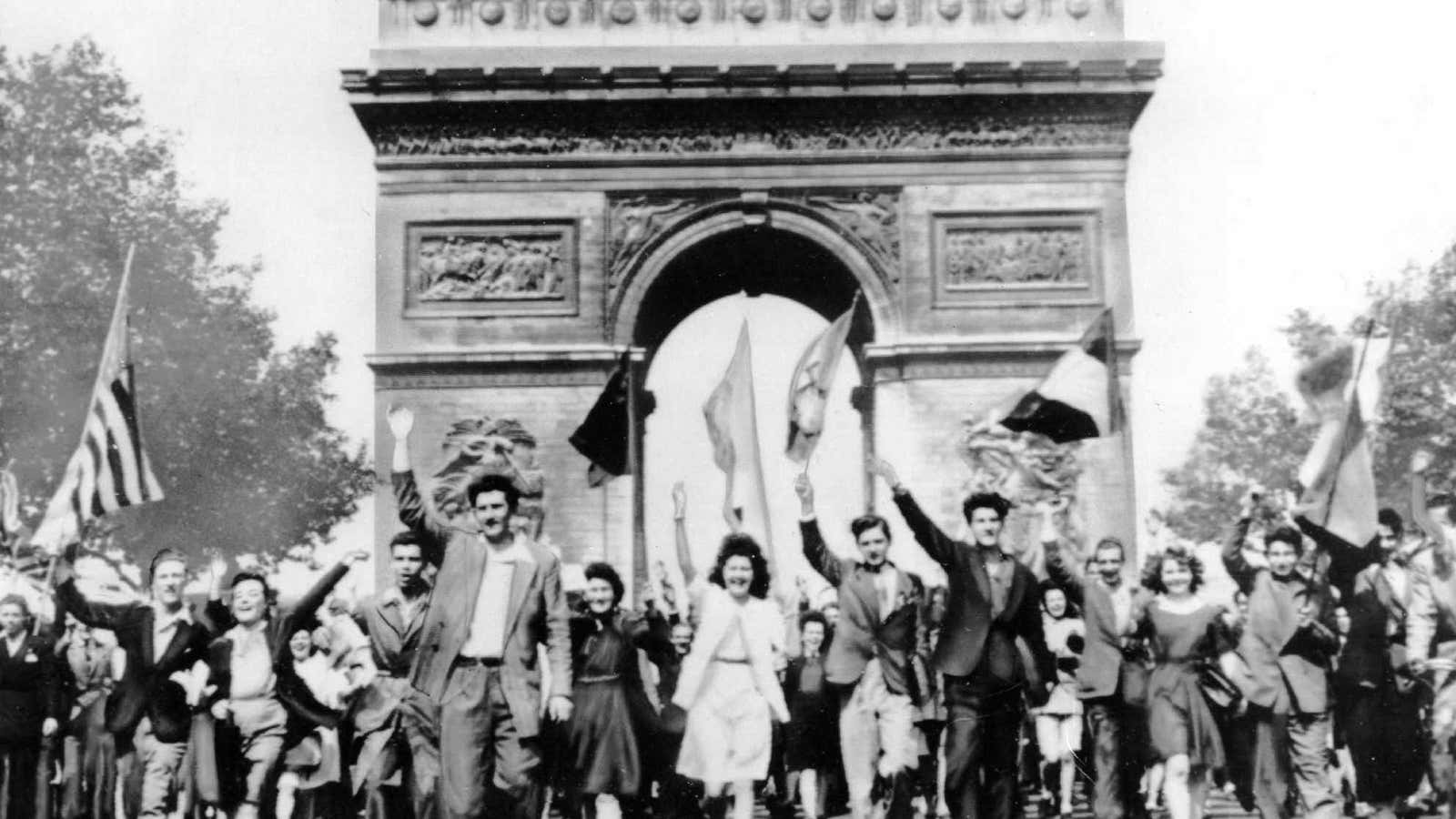 Parisians march through the Arc de Triomphe jubilantly waving flags of the Allied Nations as they celebrate the end of World War II on May 8, 1945.