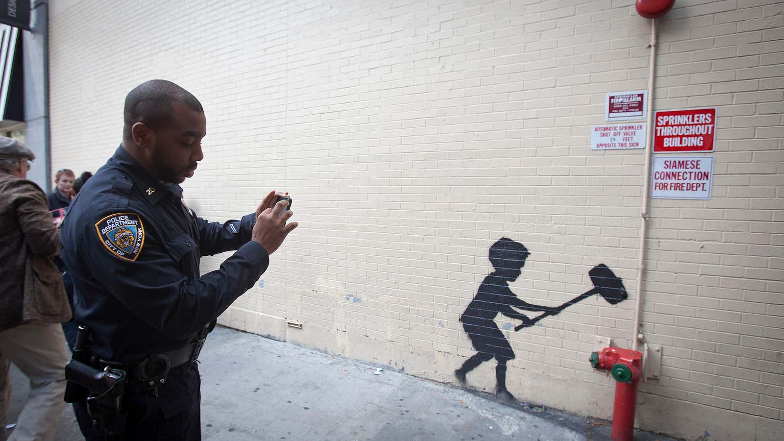 A police officer takes a photo of Banksy’s ostensibly illegal work.