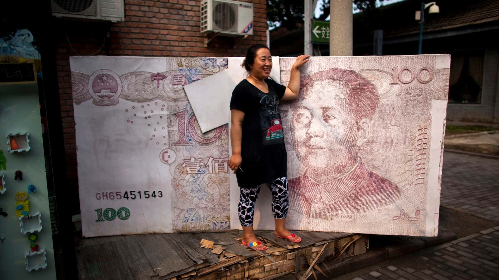 A woman poses for photos with an art installation showing a stack of renminbi banknotes in Beijing, China.