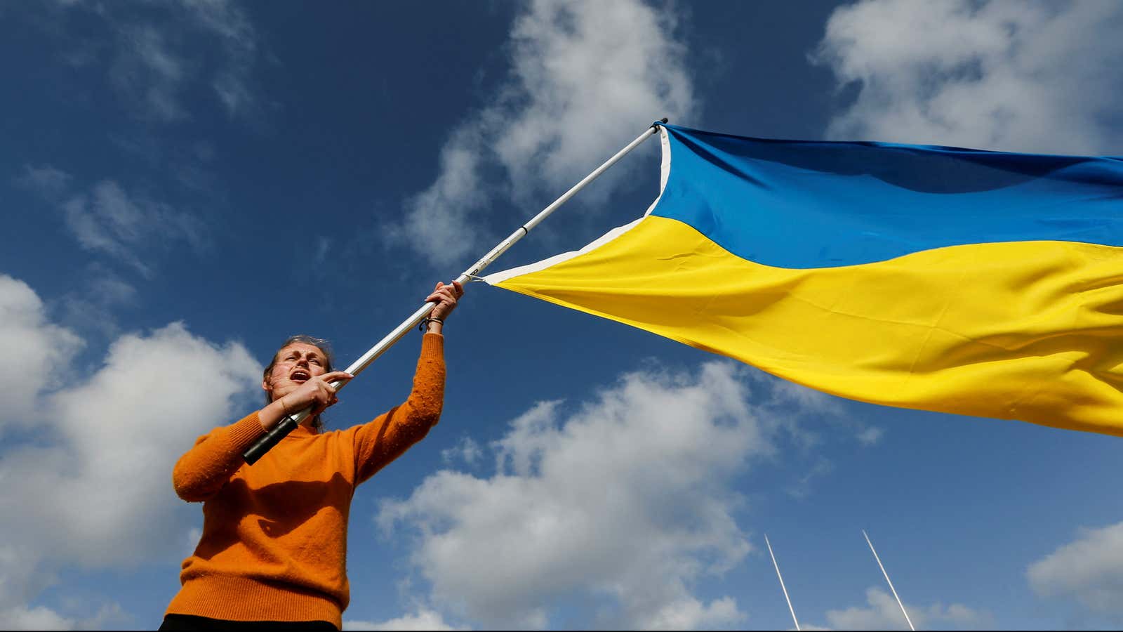 A woman waves a Ukrainian flag against the backdrop of a cloudy sky.