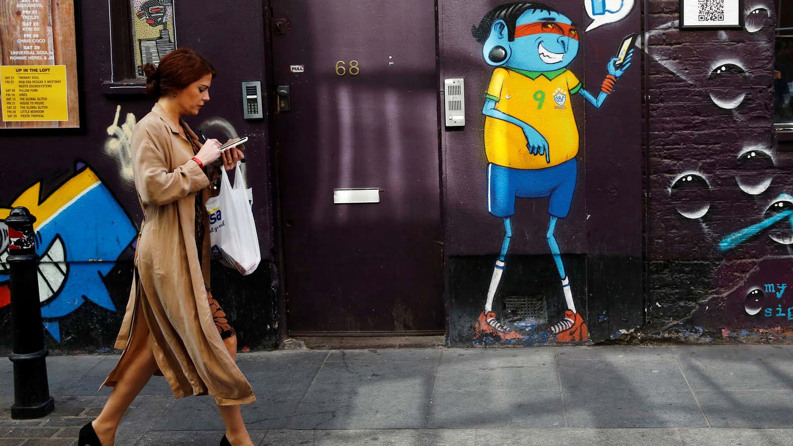 A woman looks at her mobile phone as she passes a mural in Shoreditch, London, Britain October 5, 2016. REUTERS/Stefan Wermuth  SEARCH “WERMUTH PHONES” FOR THIS STORY. SEARCH “THE WIDER IMAGE” FOR ALL STORIES. – RC13CD2F1E60