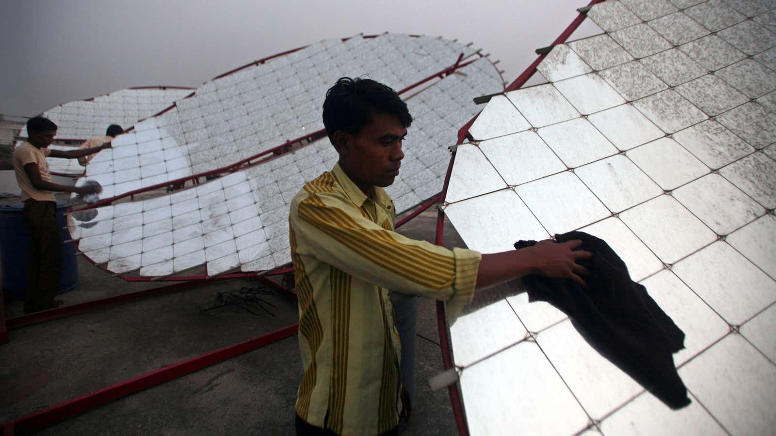 Workers clean solar concentrator panels (solar parabolic dish) at the Tapi solar food processing unit at Kapodra village, about 350 km (220 miles) south of…
