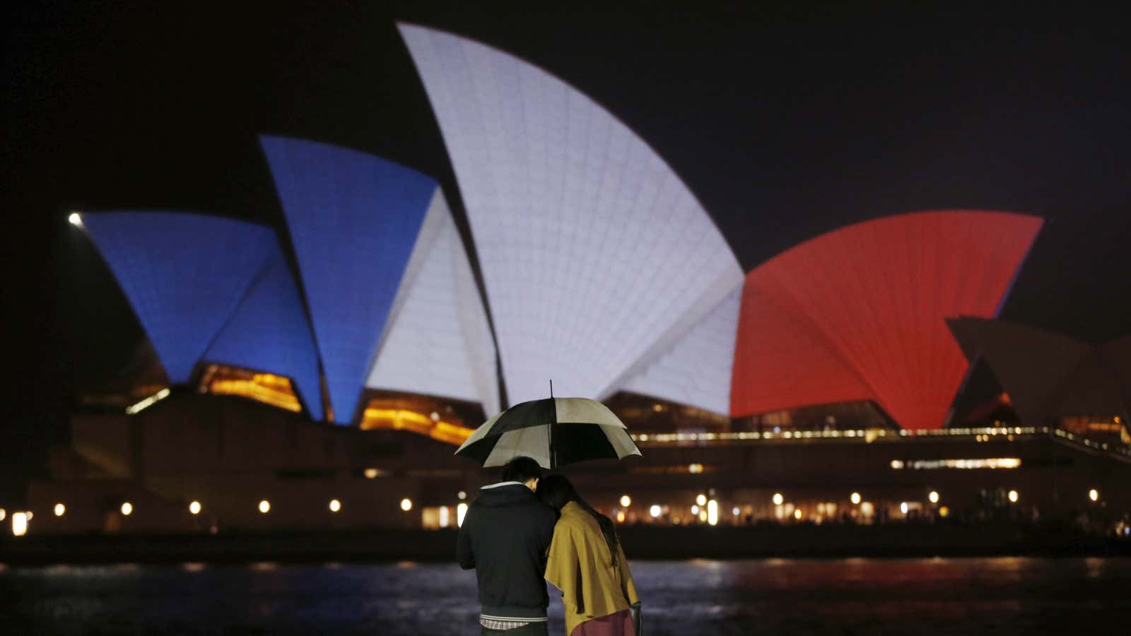 A couple stands in the rain as the blue, white and red colors of France’s national flag are projected onto the sails of Sydney’s Opera House in Australia on Nov. 14.