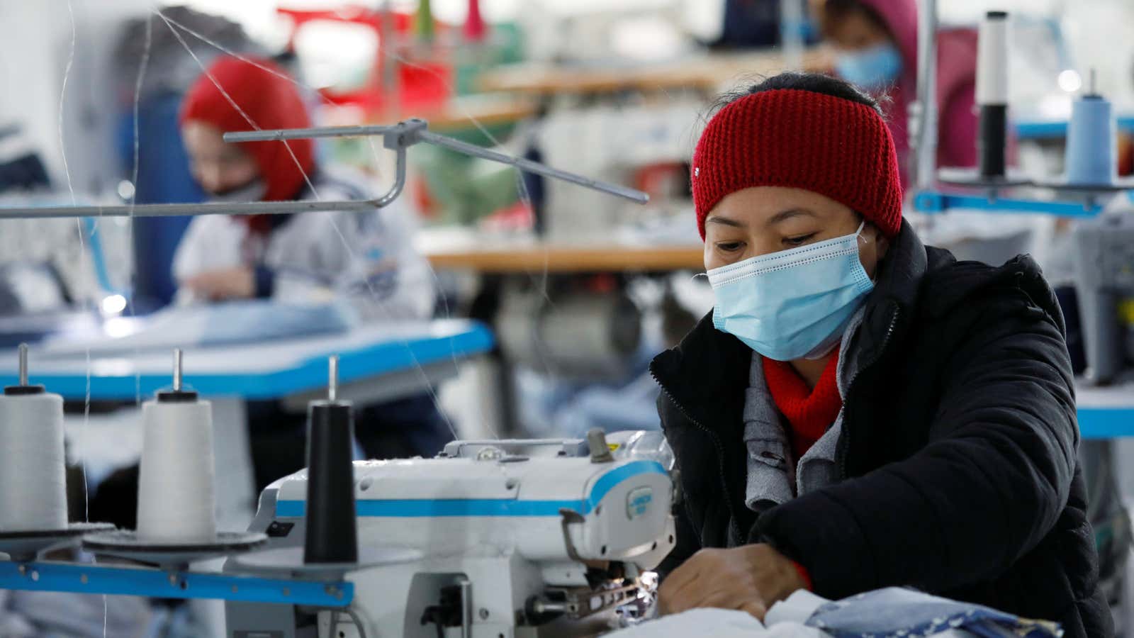 A woman wearing a surgical mask sits at a sewing machine in a Vietnamese factory.