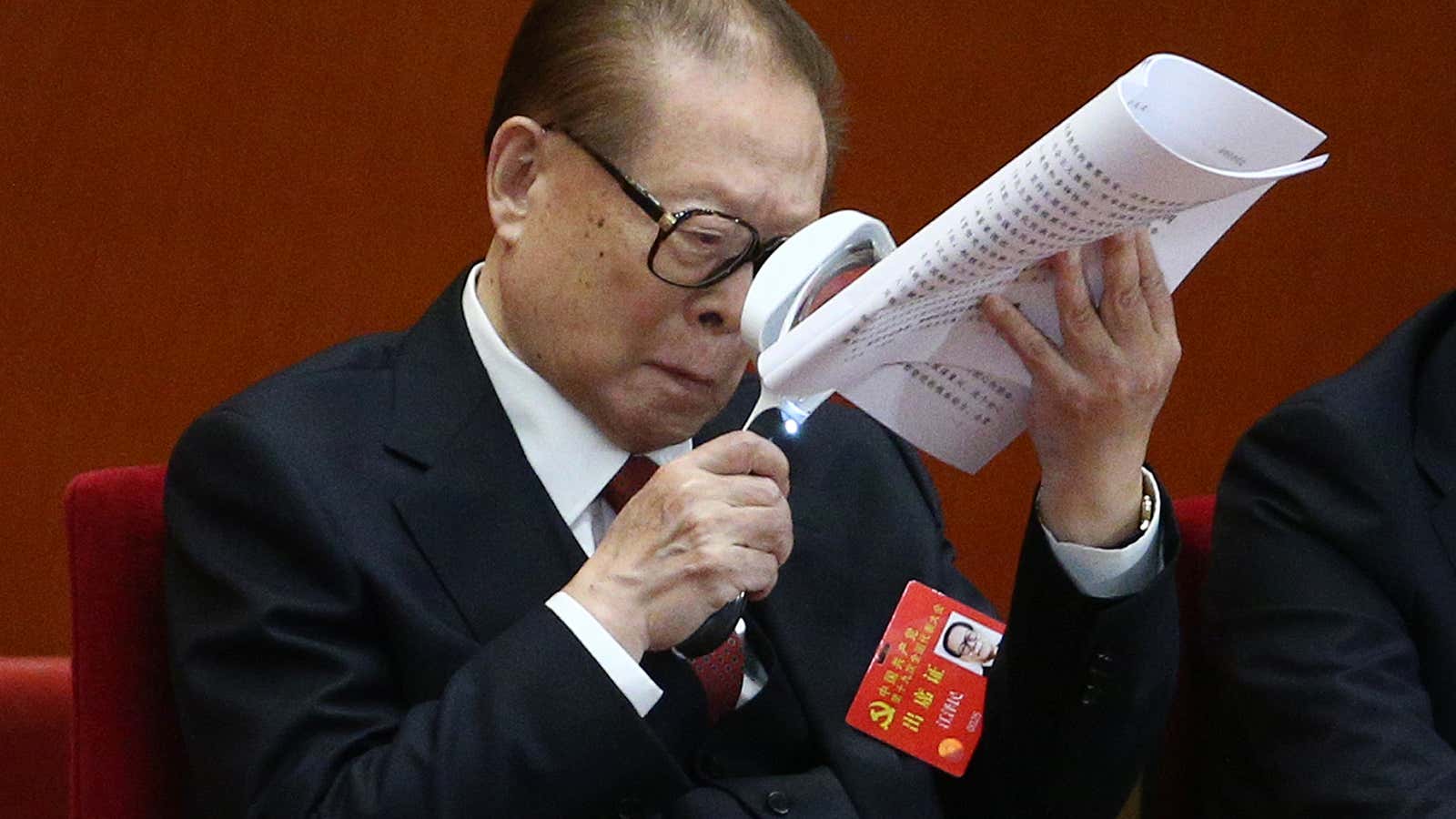 Former Chinese president Jiang Zemin holds a magnifying glass while reading a document.