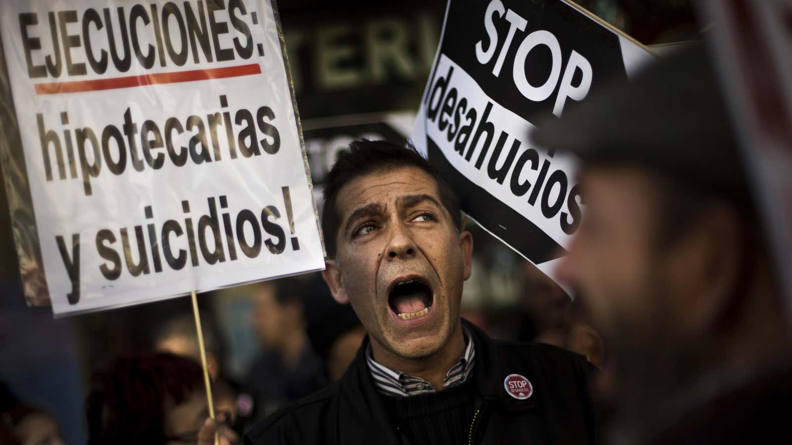 A demonstrator in Madrid holds up a sign that reads “Executions, evictions and suicides” during a protest in front of the conservative party PP headquarters.