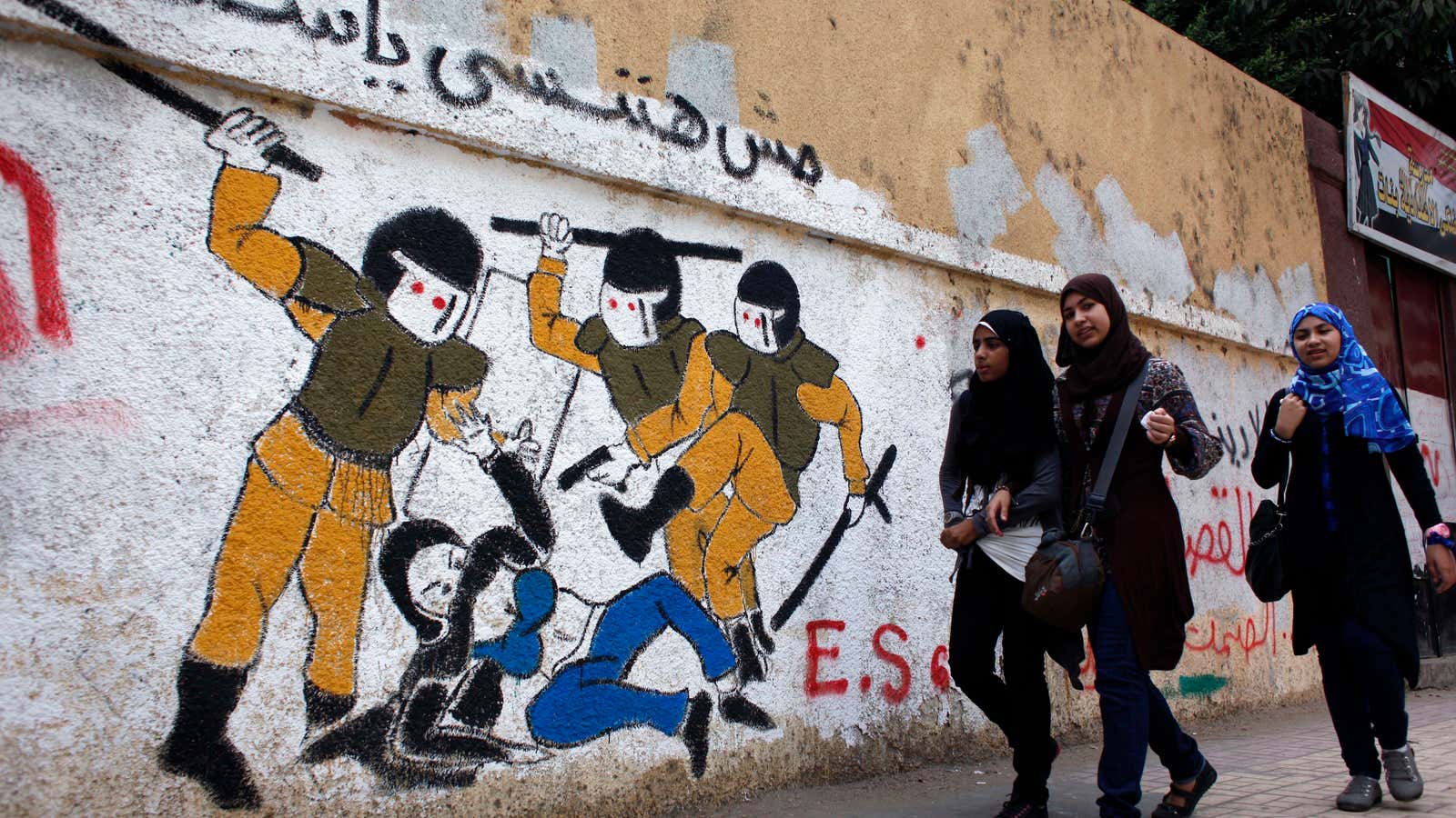 Egyptian girls walk past a mural in Tahrir Square, Cairo.