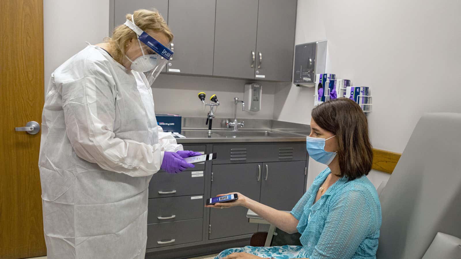 A doctor users her phone to scan the screen a patient’s smartphone, which displays a large QR code.