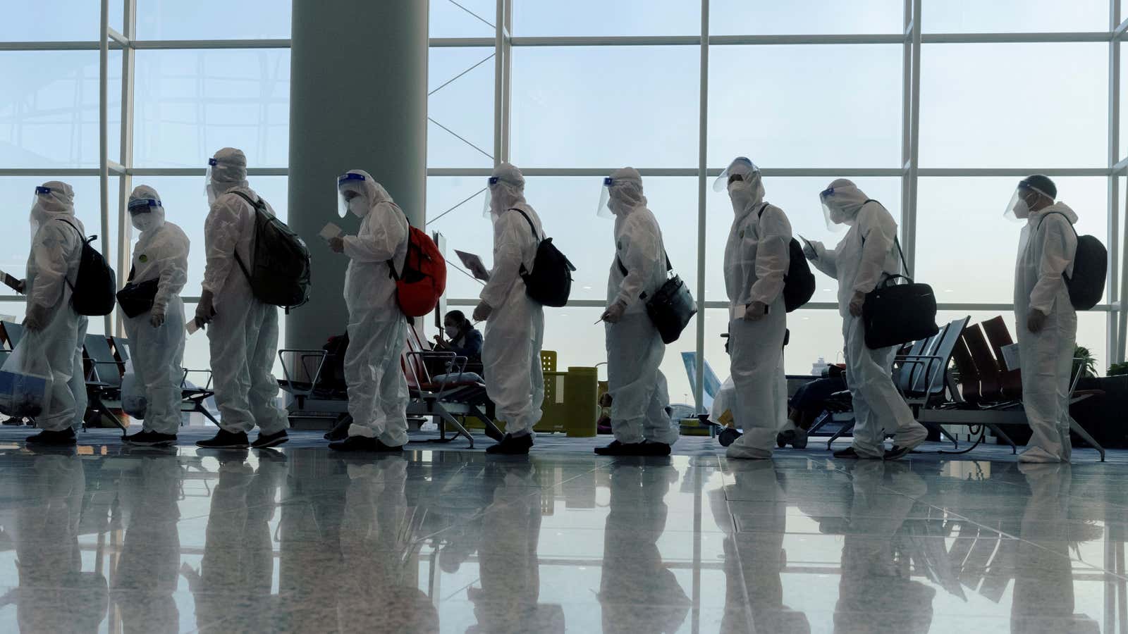 Passengers wearing protective suits (PPE) line up to board their plane for an international flight at Hong Kong airport in July 2021.