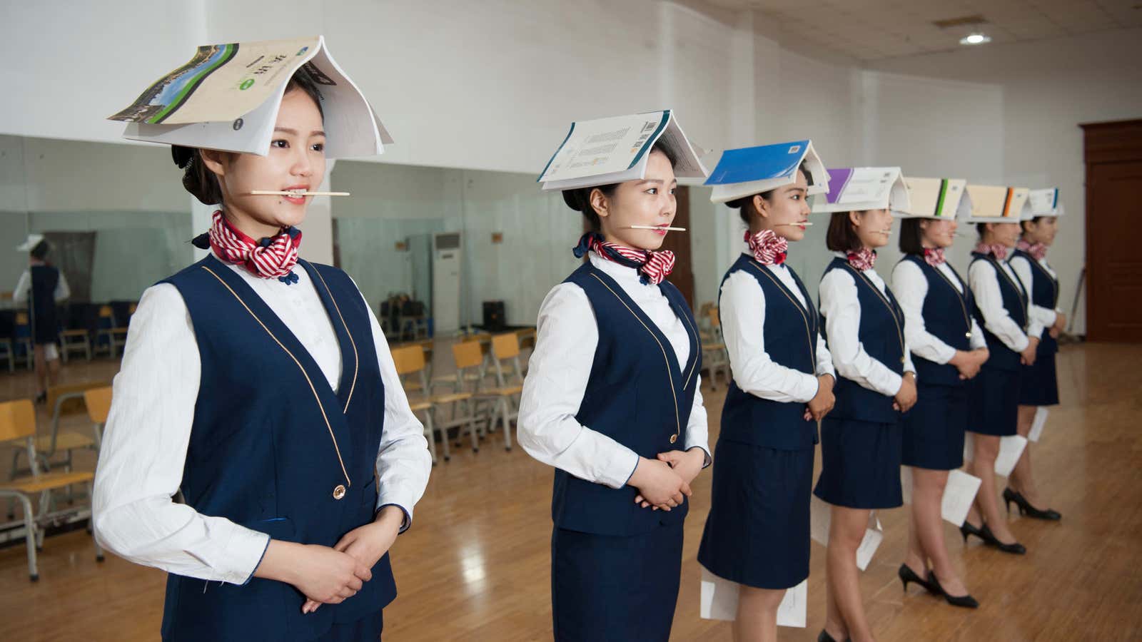 Students training to be flight attendants hold books on their heads, chopsticks in their mouths, and papers in a standing posture practice in China.