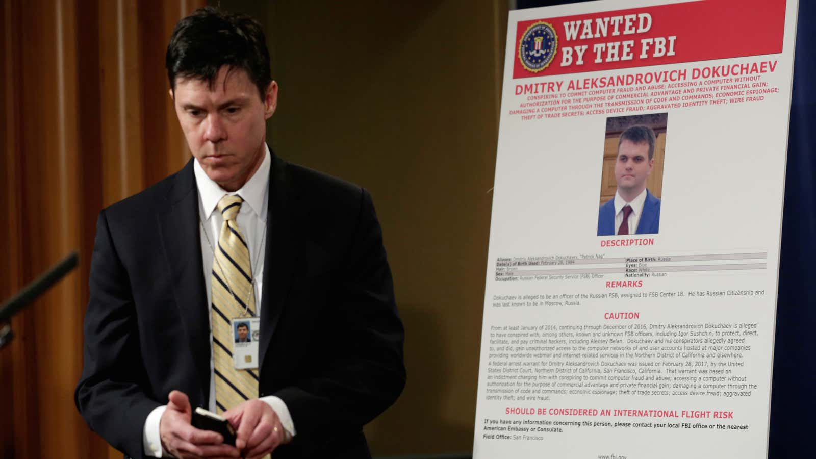 A Department of Justice staffer walks past a poster of a suspected Russian hacker.