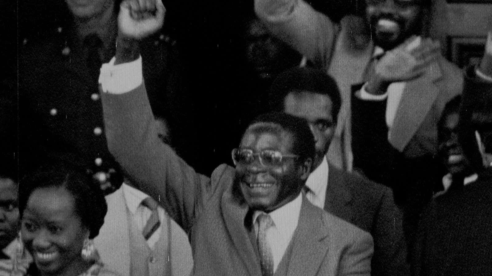 Zimbabwean Premier Robert Mugabe gives a triumphant salute as he emerges from parliament following its official opening, May 14, 1980.  At right is Mugabe’s wife Sally.