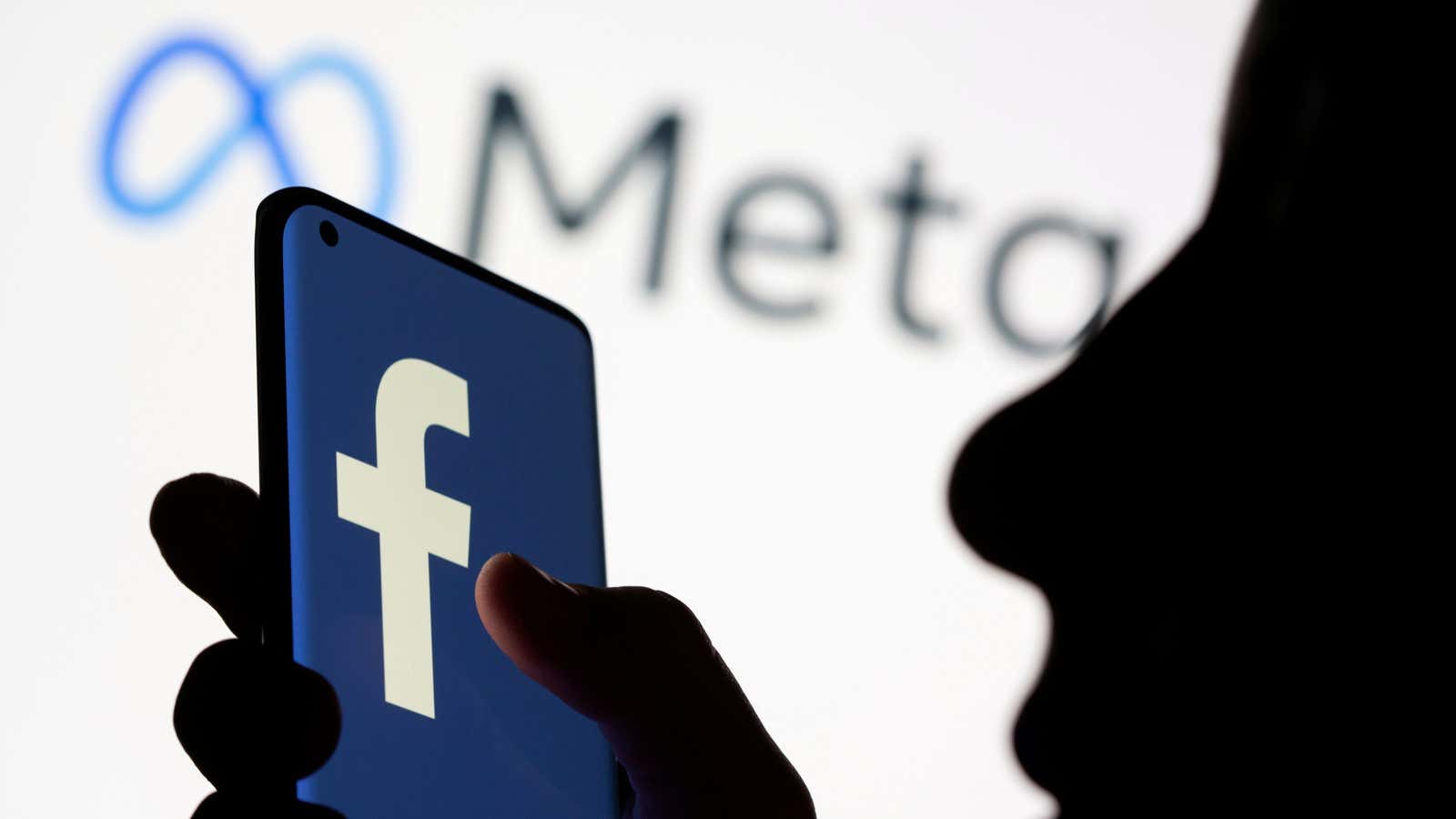 FILE PHOTO: FILE PHOTO: Woman holds smartphone with Facebook logo in front of a displayed Facebook’s new rebrand logo Meta in this illustration picture taken…