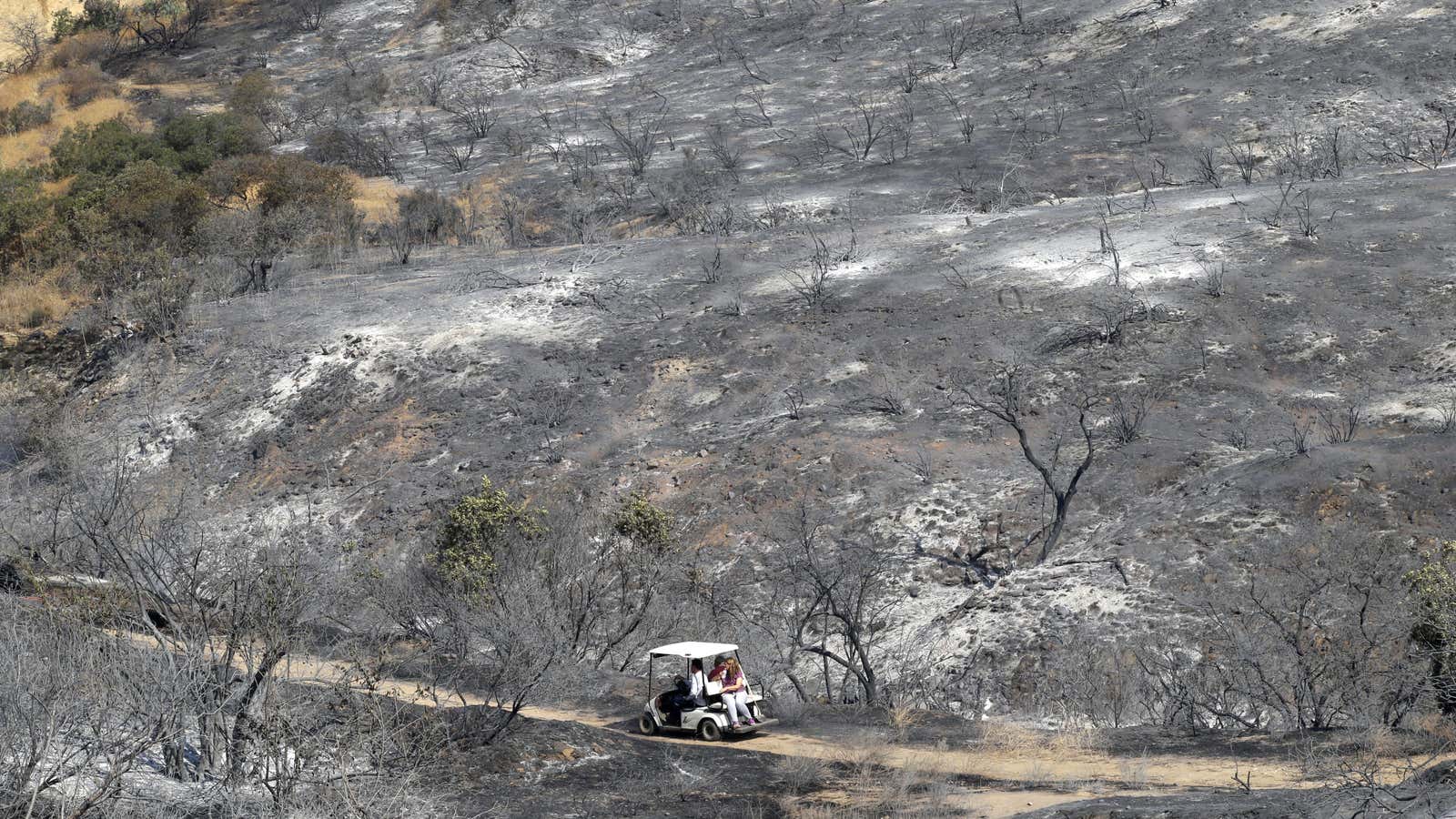 Residents ride a golf cart as they survey the damage caused by the La Tuna fire.