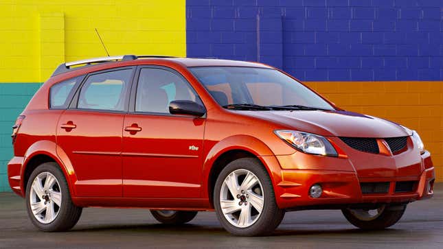 A photo of a red Pontiac Vibe parked in front of a colorful building. 