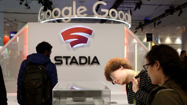 A photo shows two people looking at a Stadia controller with a large Google logo behind them.