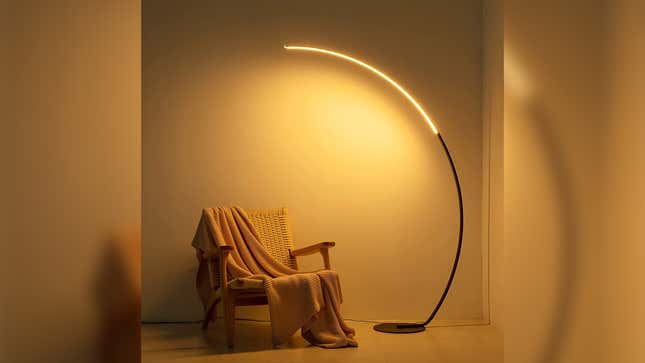 The arc floor lamp illuminated a chair with a blanket.