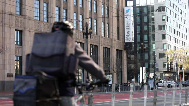 A person on a bicycle rides down the street in front of the California Twitter offices with the big Twitter sign out front.