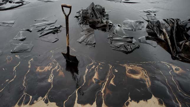 A shovel sits in oil-covered sand.
