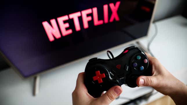 A person holds a game controller in front of a television while Netflix loads.
