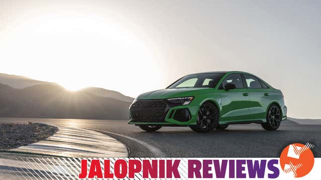 Green 2022 Audi RS 3 on track with mountain range and setting sun in background.