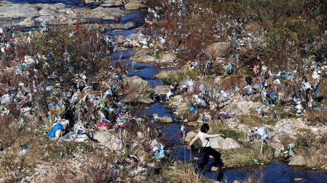 A woman crosses a stream running through land littered with plastic wastes in Shangxi village, eastern China’s Zhejiang province.
